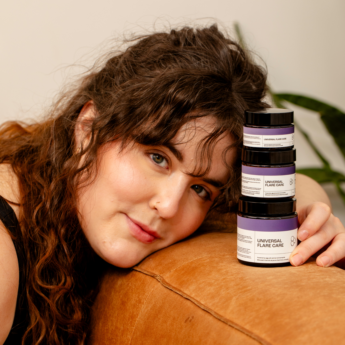 Model resting on couch next to stack of Universal Flare Care sensitive skin cream jars
