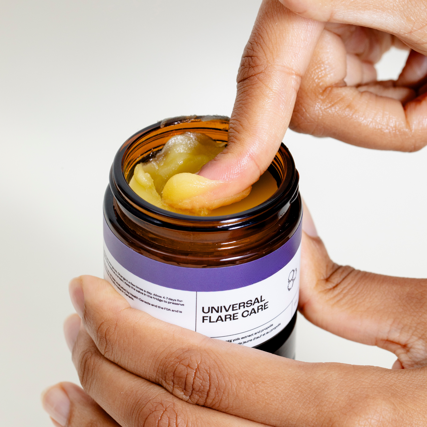 Hand scooping Universal Flare Care sensitive skin cream from jar showing thick yellow balm texture
